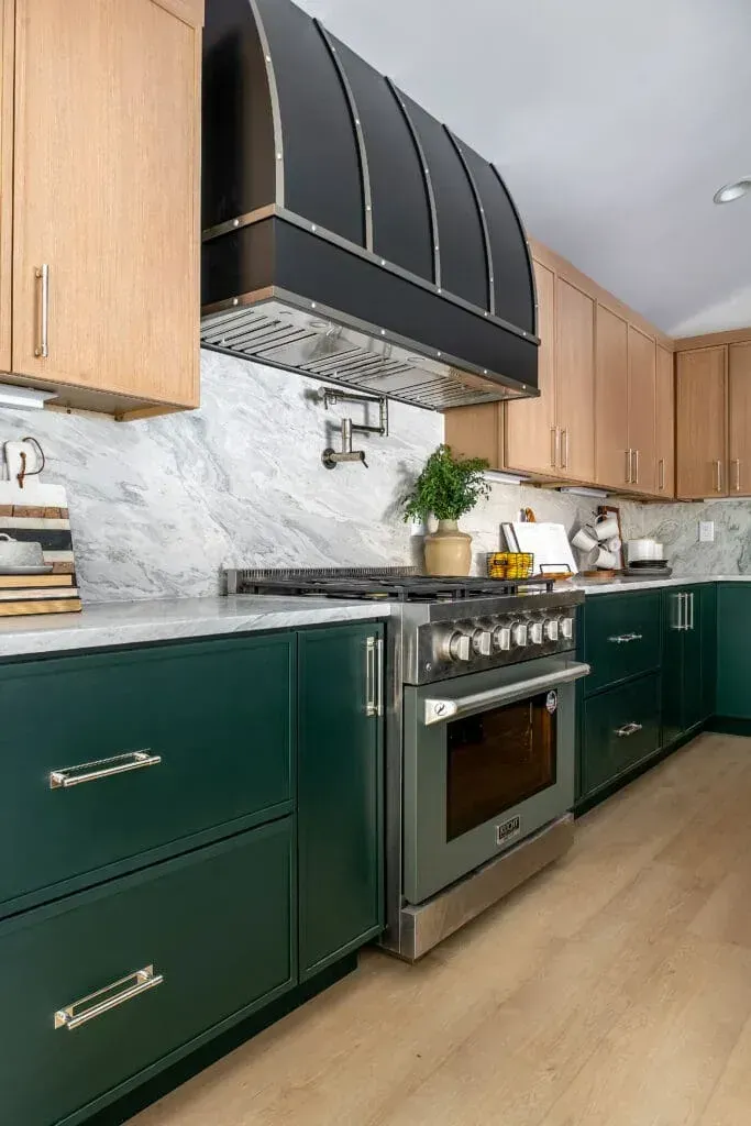 Green and wood-toned kitchen with stainless steel appliances, black hood, and marble backsplash.