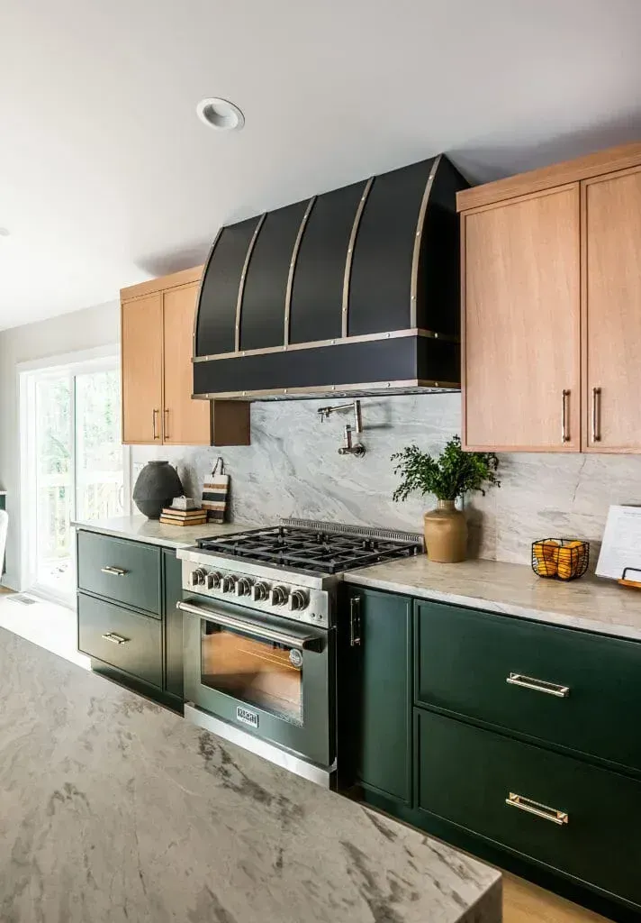 Modern kitchen with two-tone cabinets: light wood and dark green. Black range hood and stainless steel oven.