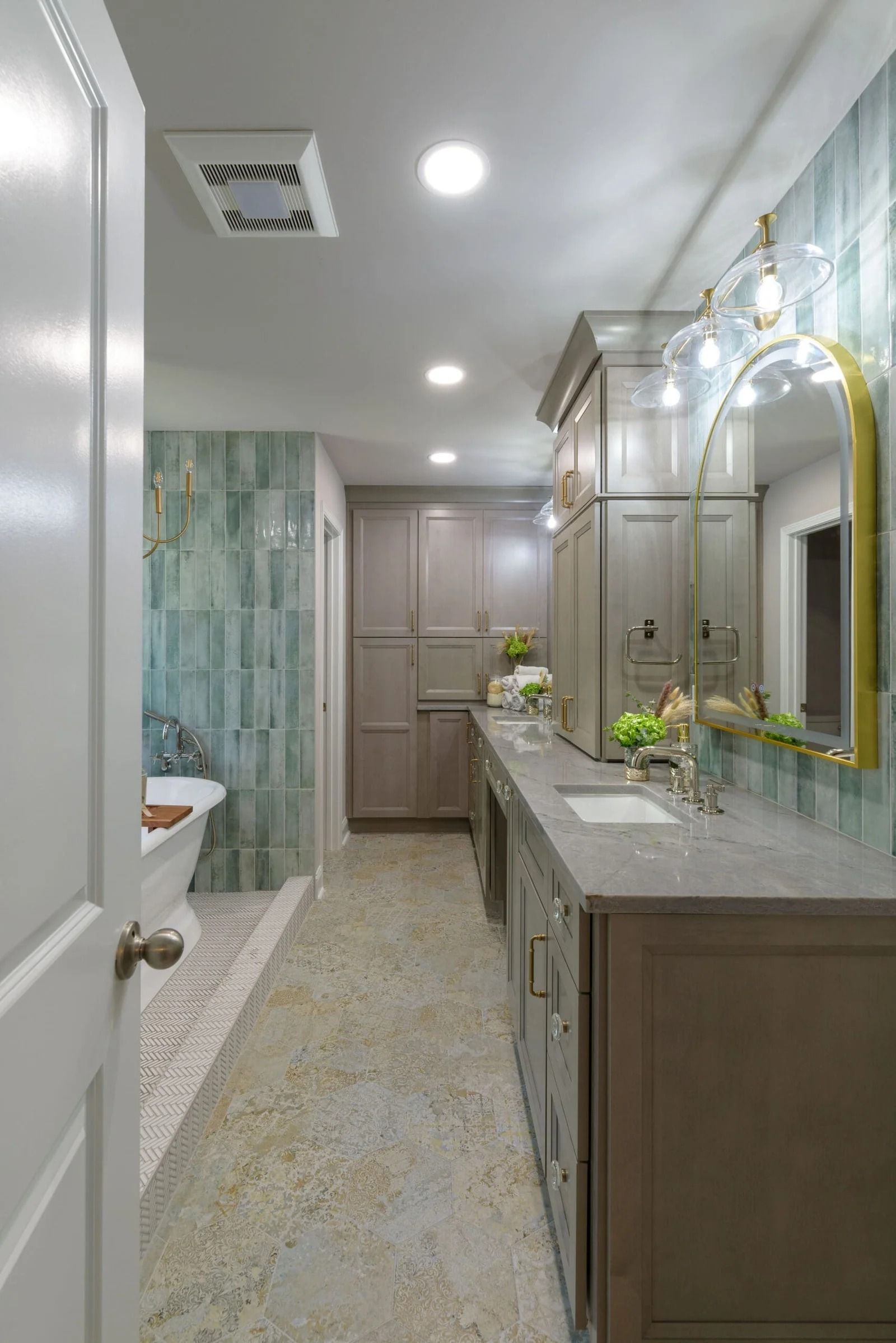 Long, narrow bathroom with light-gray cabinets, green tiled wall, and a gold-framed mirror.