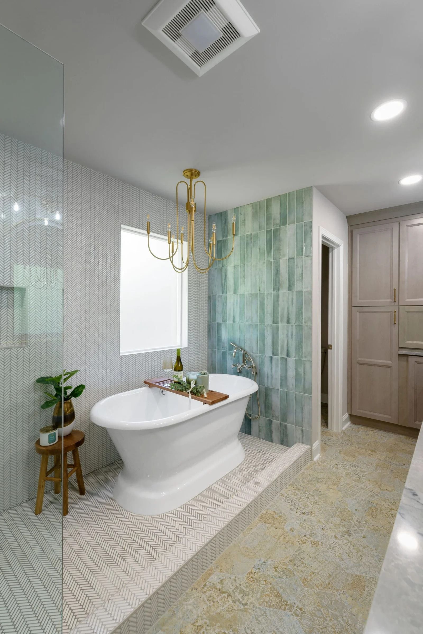 Elegant bathroom with a white freestanding tub, teal accent tile, and gold chandelier.