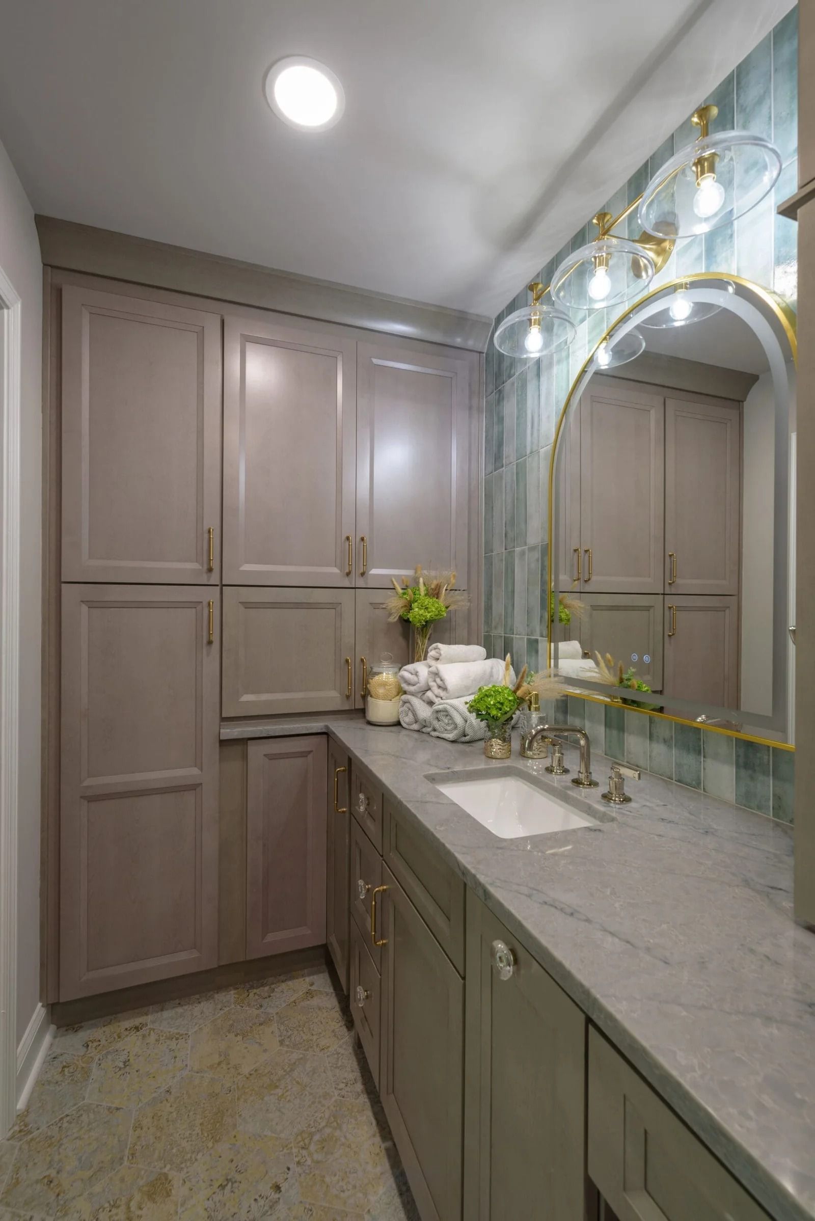 Bathroom with gray cabinets, countertop, and mirror with gold frame. Bright lights and towels on display.