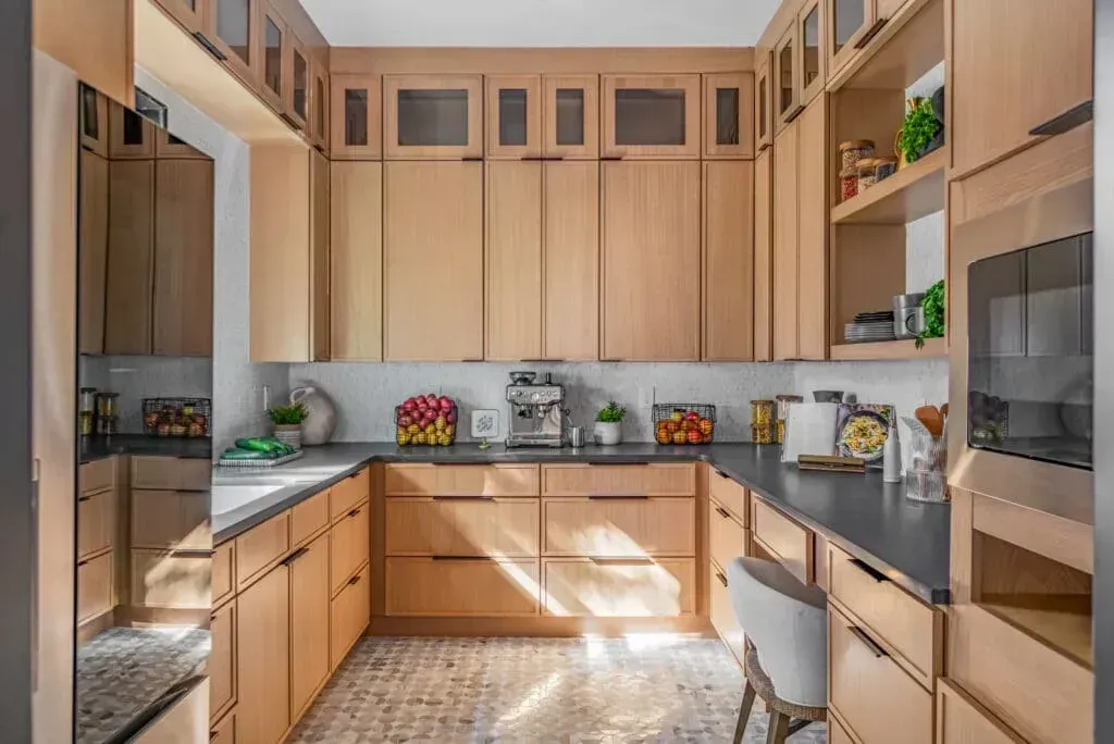 U-shaped kitchen with light wood cabinets, dark countertops, and patterned floor.