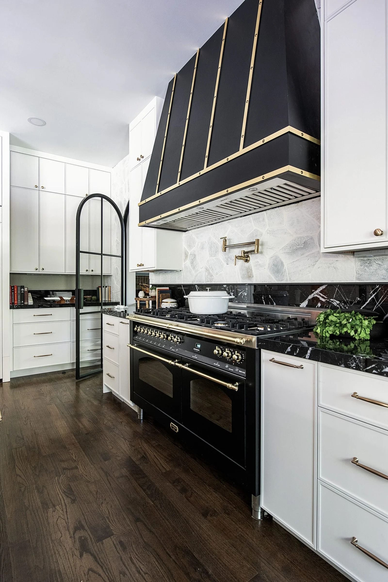 Kitchen with black range, hood, white cabinets, dark wood floor.