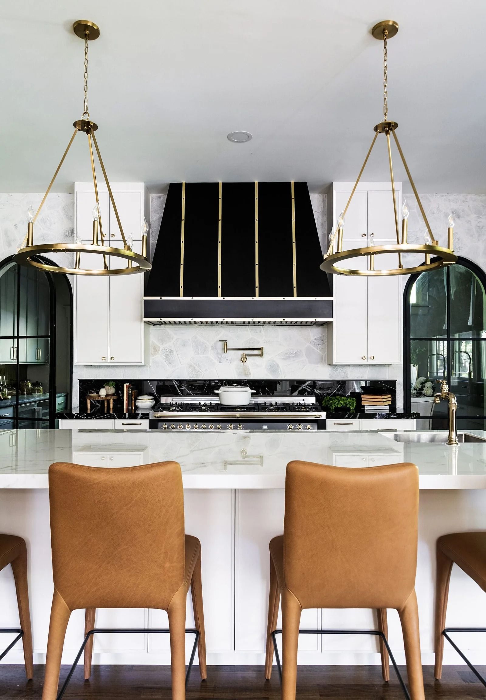 Kitchen with marble countertops, black stove hood, gold lighting, and brown leather bar stools.