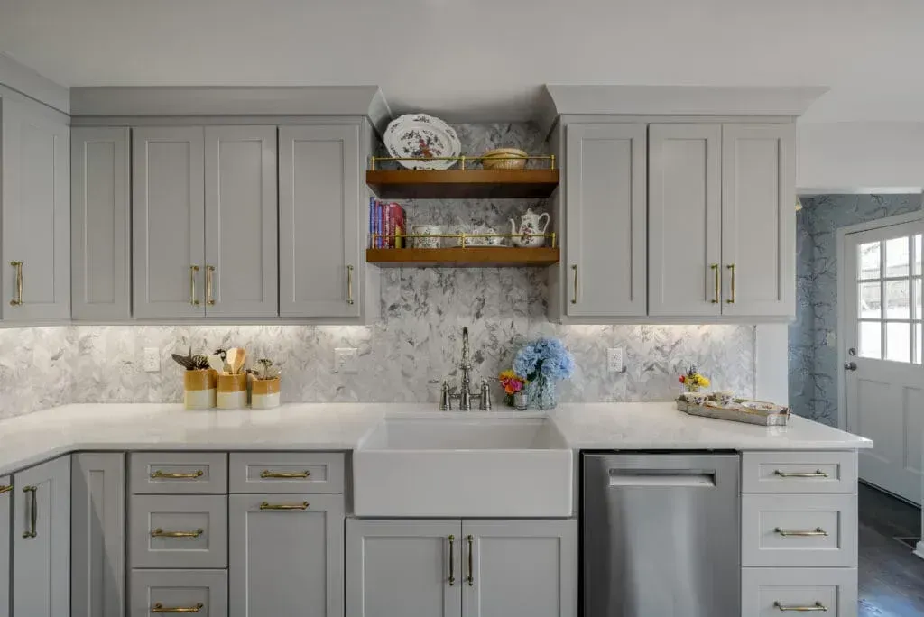 Gray kitchen with marble backsplash, farmhouse sink, and wooden shelves displaying dishes.
