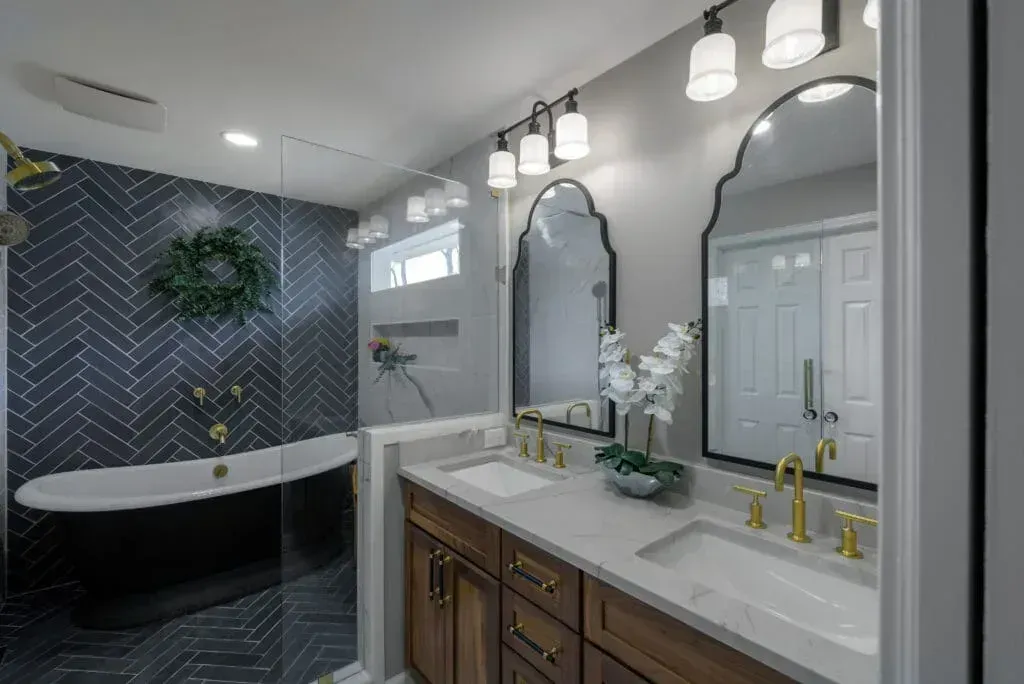 Bathroom with dark blue herringbone tile, black tub, double vanity, and arched mirrors.