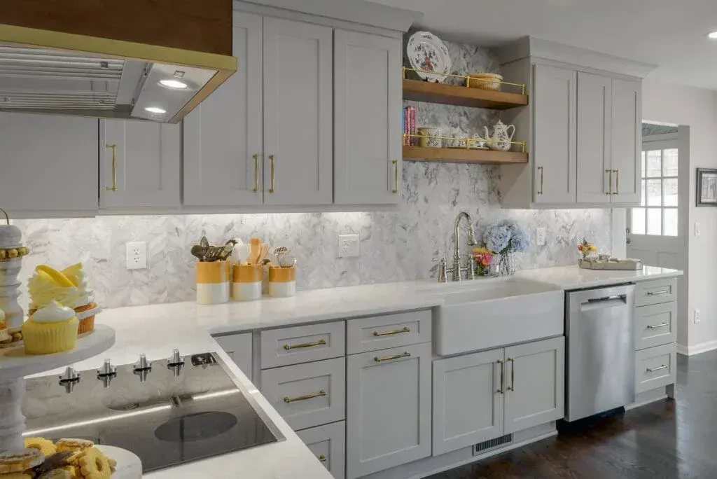 Gray kitchen with white countertops, marble backsplash, gold hardware, and open shelving.
