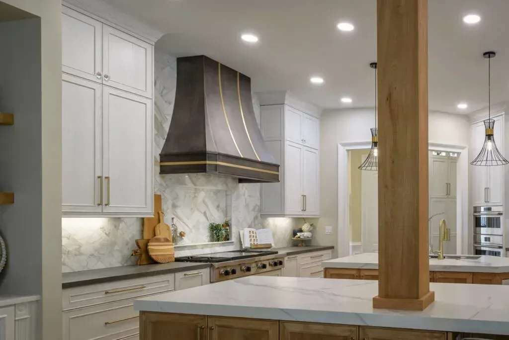 Stylish kitchen with white cabinets, marble backsplash, and a dark range hood with gold trim.