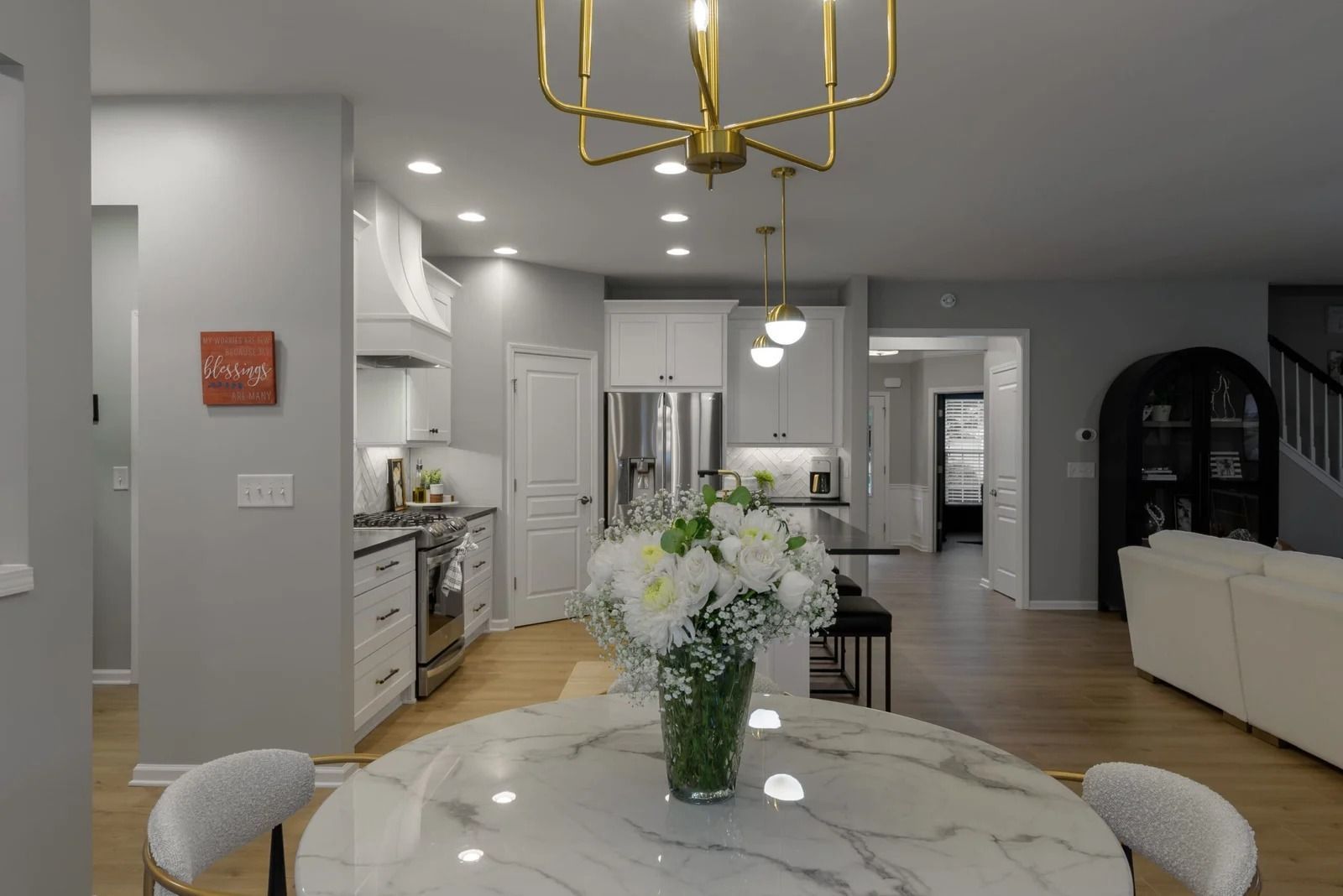A modern kitchen and dining room with white cabinets, marble table, and gold chandelier.