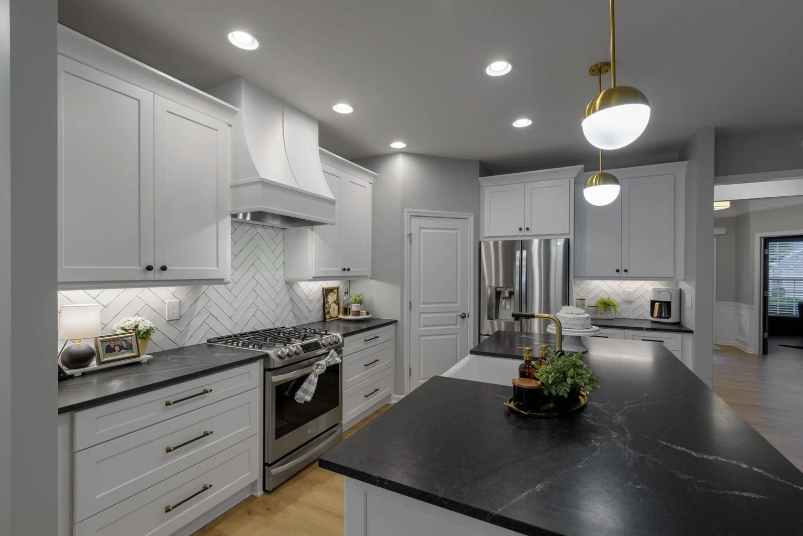 Modern white kitchen with black countertops, stainless steel appliances, and pendant lights.