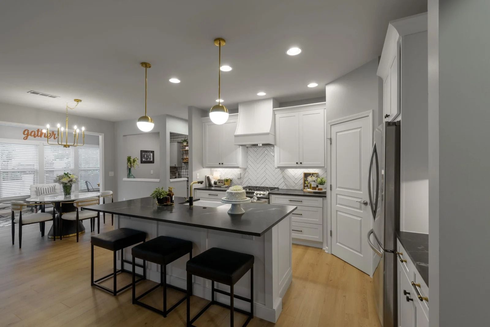 Modern kitchen with island, white cabinets, gold light fixtures, and dining area.
