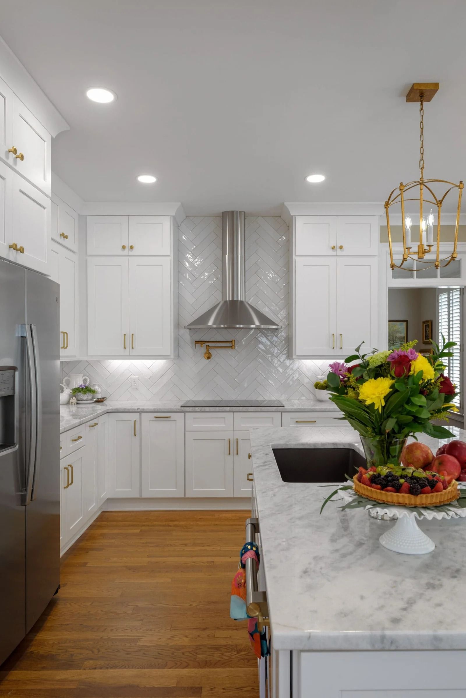 White kitchen with stainless steel appliances, marble countertops, and a flower arrangement on an island.