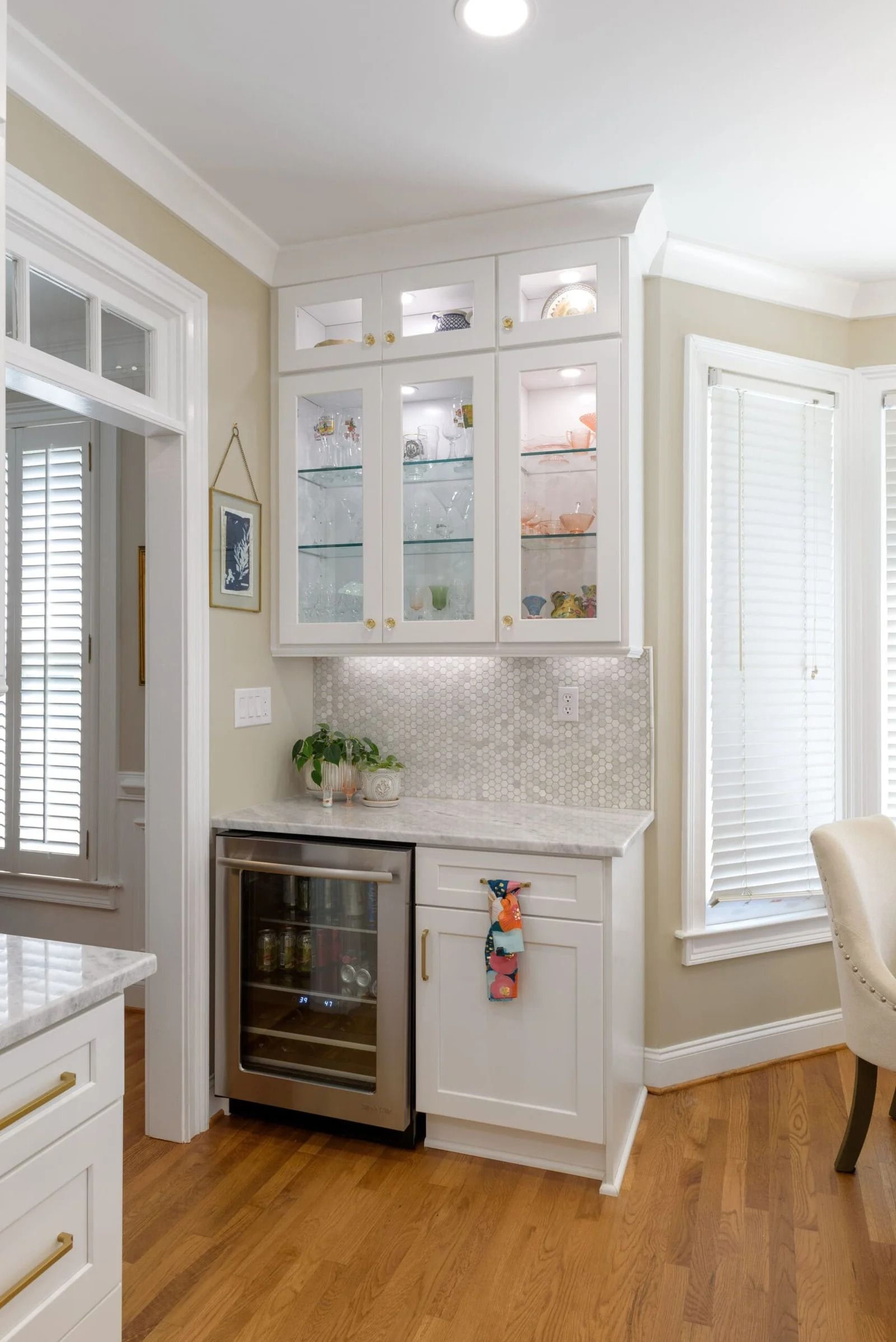 White built-in bar area with a wine fridge, glass-front cabinets, and a white backsplash in a dining area.