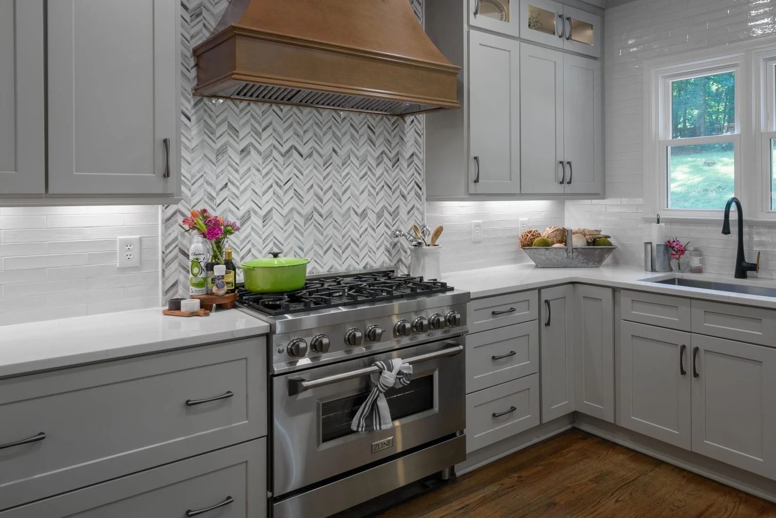 Gray kitchen with stainless steel appliances, a copper hood, and a marble backsplash.