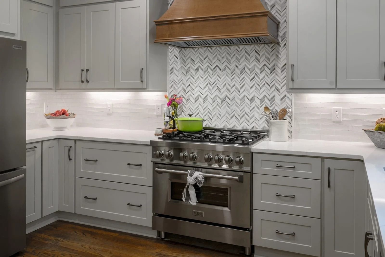 Gray kitchen with stainless steel appliances, light countertops, and a herringbone backsplash.