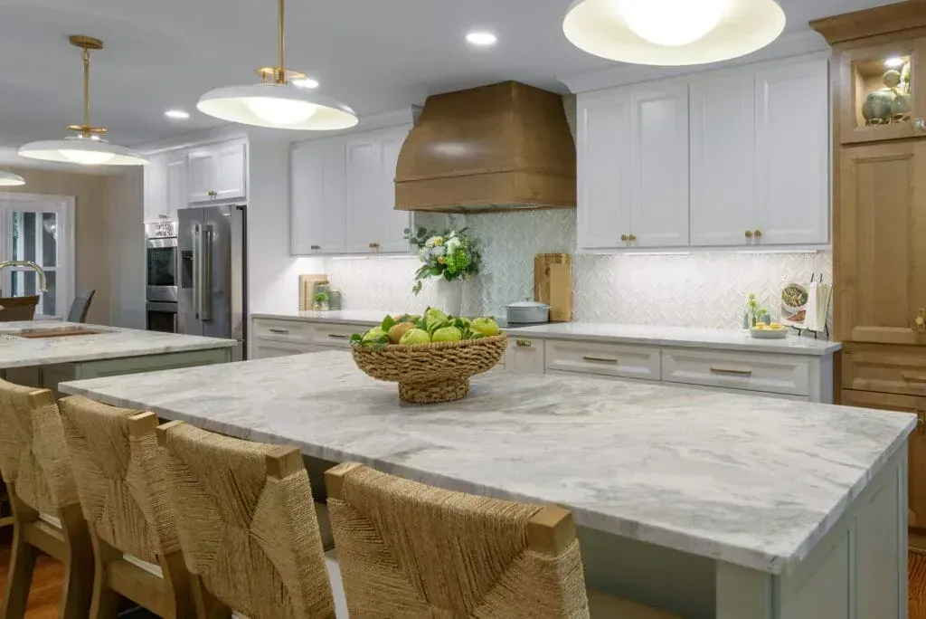 Kitchen with white cabinets, a large island with woven stools, and a wooden range hood.