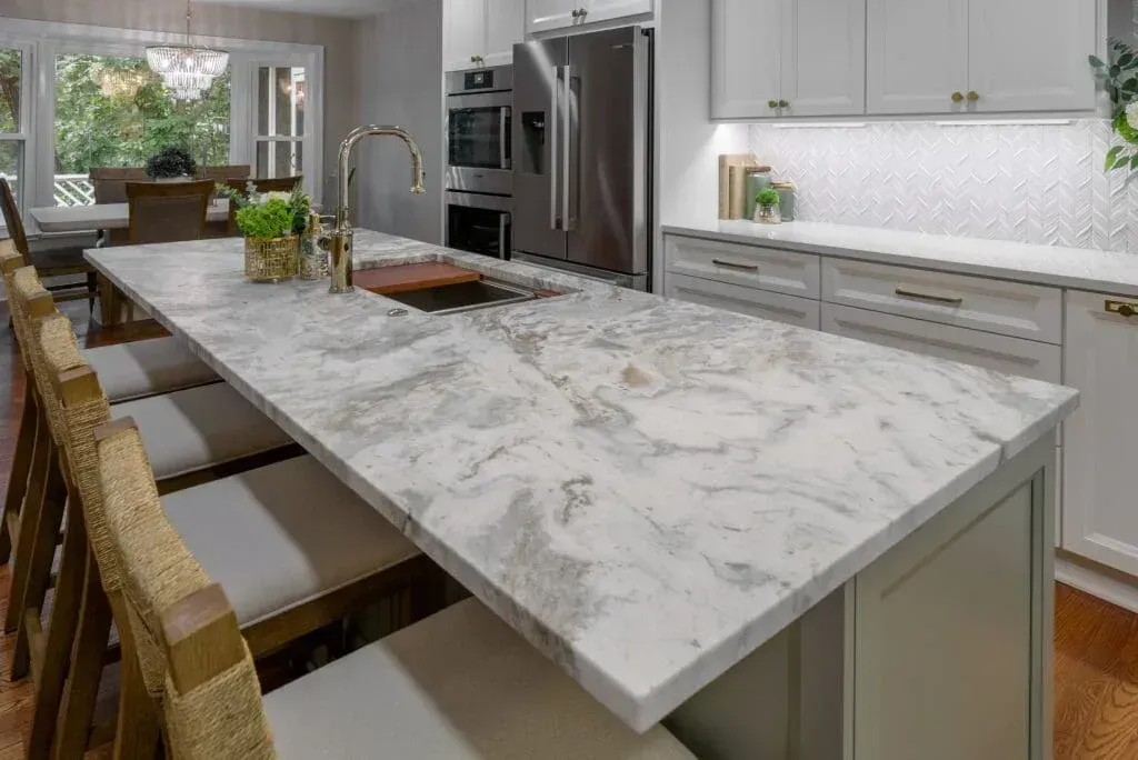 Kitchen island with white and gray marble countertop, seating, and gold fixtures.