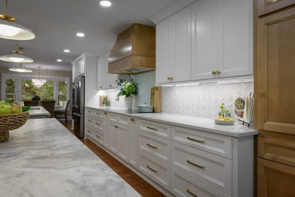 White kitchen with marble countertop, wood hood, and white cabinets with brass hardware.
