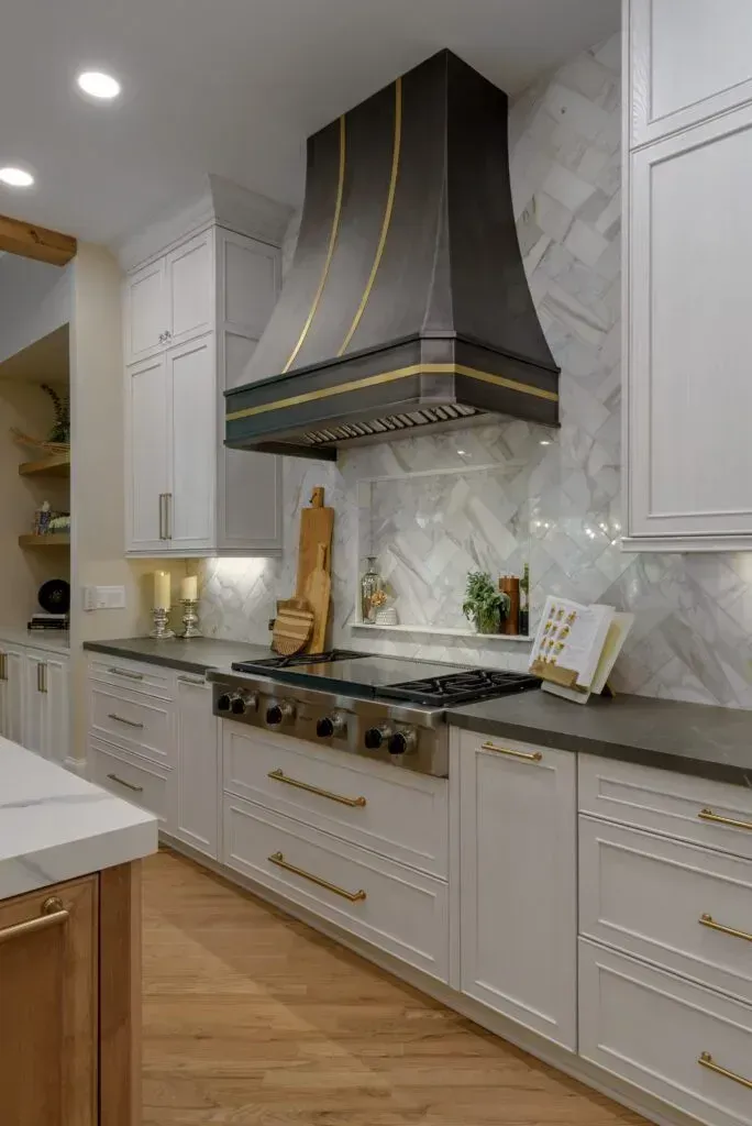 Elegant kitchen with white cabinets, dark range hood, and marble backsplash.