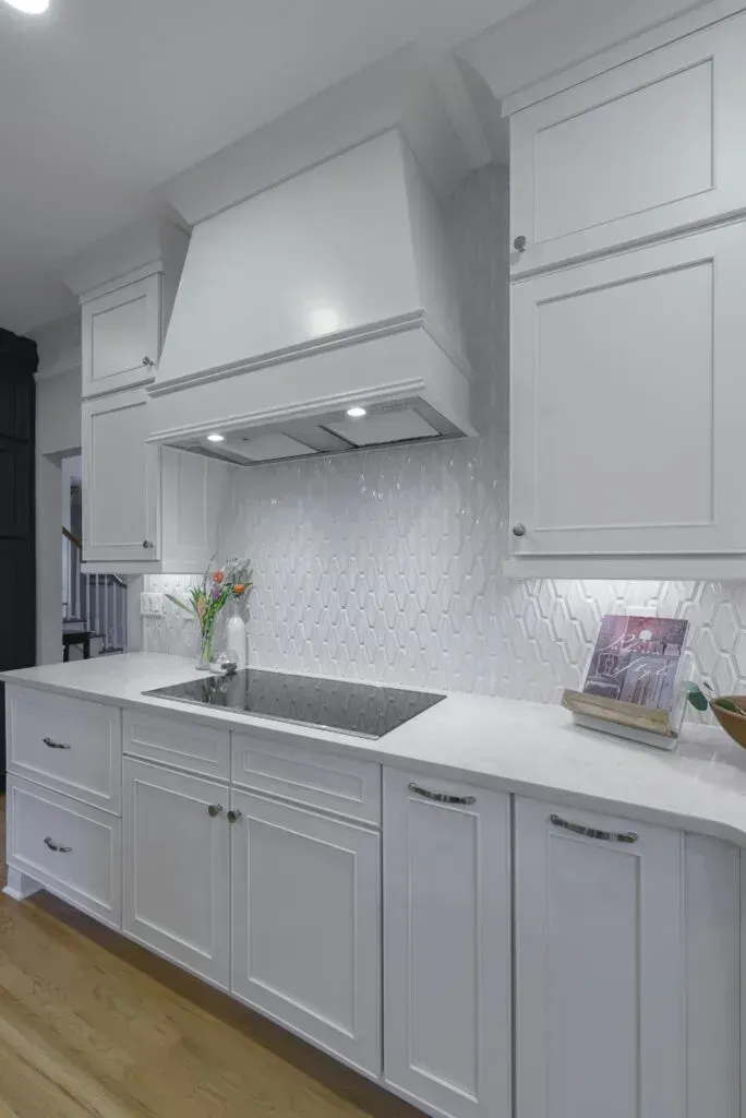 White kitchen with cabinets, range hood, and white backsplash.