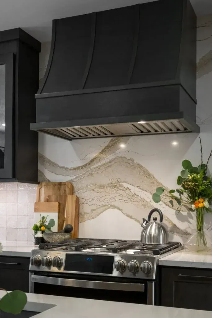 Black kitchen range hood above a gas stove with a unique marble backsplash.