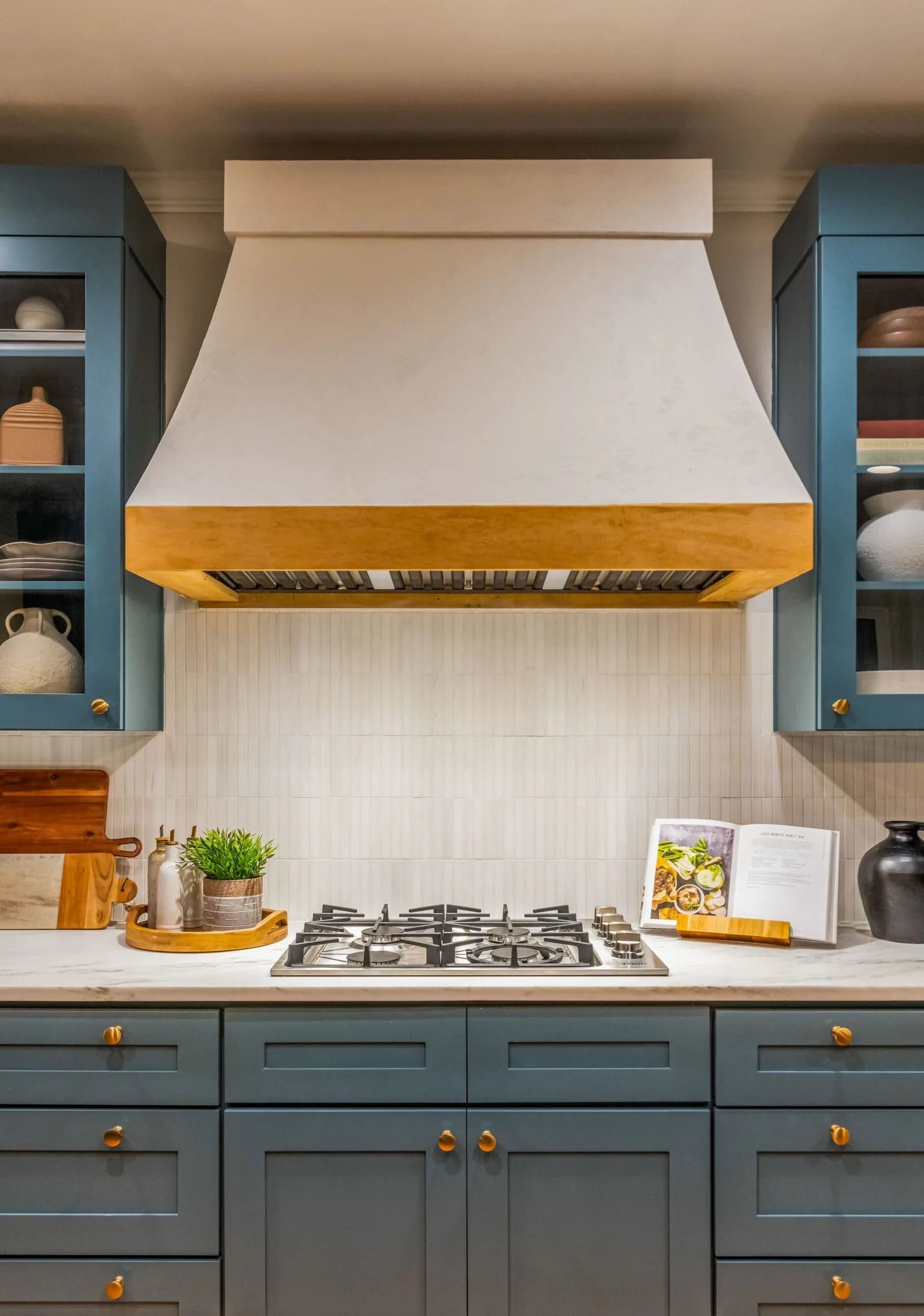 Blue kitchen with white range hood over gas stovetop, flanked by blue cabinets, gold hardware.