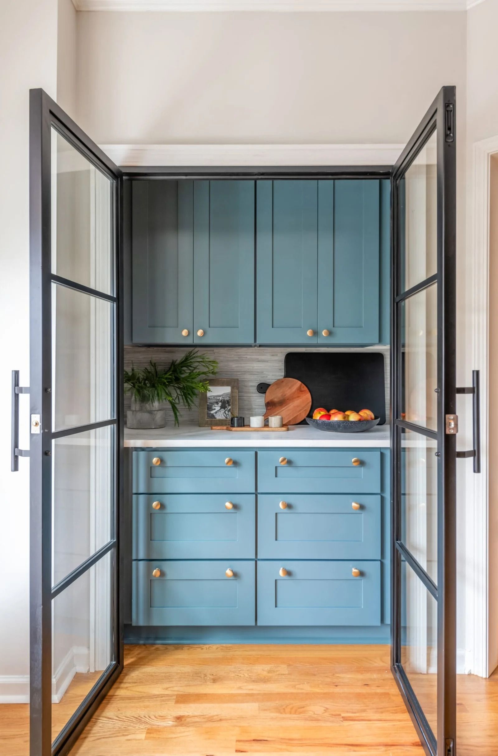 Blue pantry with glass doors and wood floor.