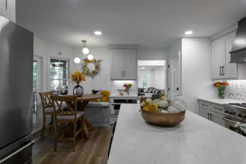 Modern kitchen with light gray cabinets, island, and dining table, decorated with fall colors.