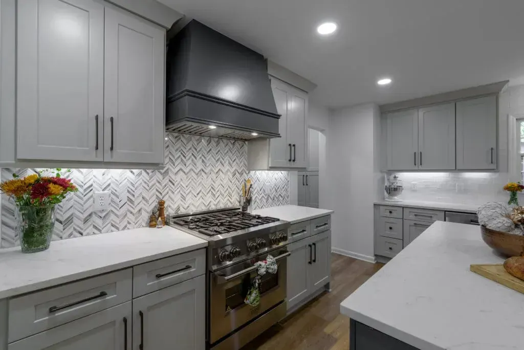 Gray kitchen with stove, range hood, cabinets, white countertops, and backsplash.