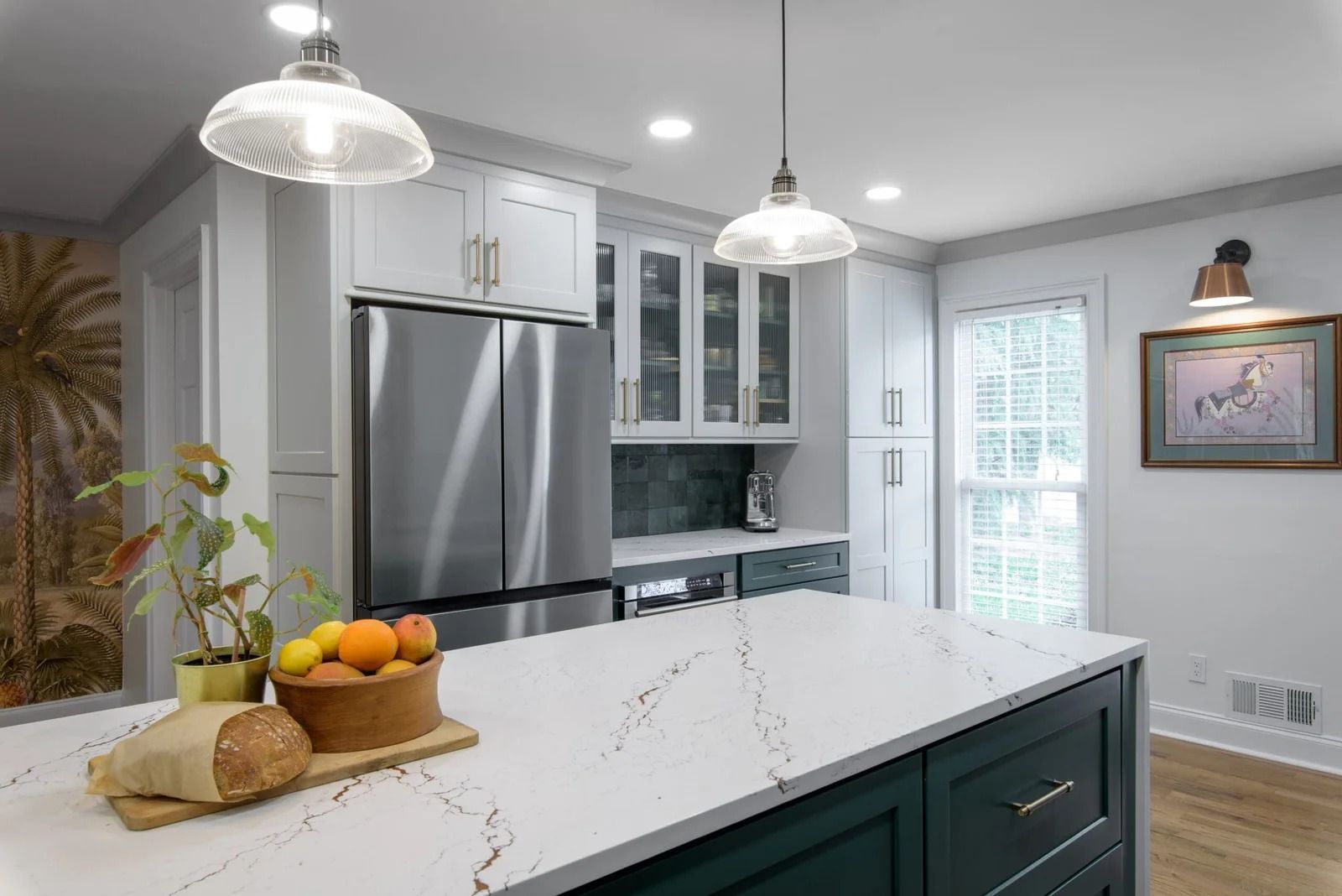 Modern kitchen with island, white countertops, and dark green cabinets. Stainless steel fridge, glass-door cabinets.