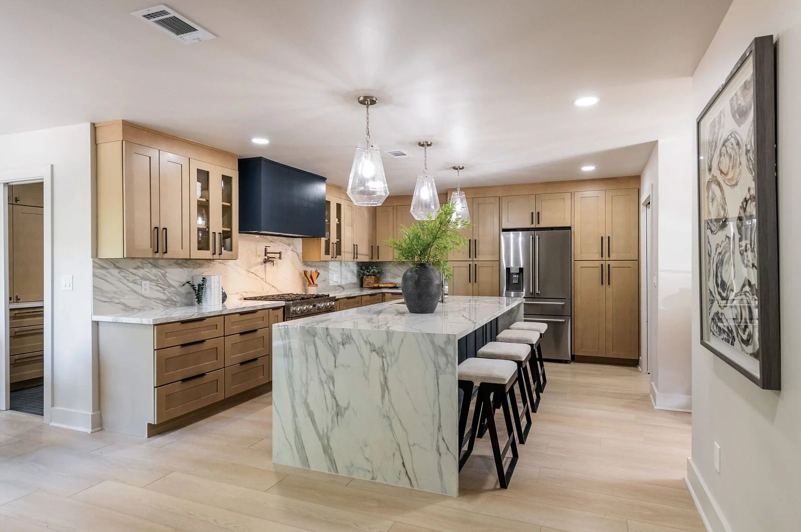 Modern kitchen with wood cabinets, marble island, stainless steel appliances, and pendant lights.