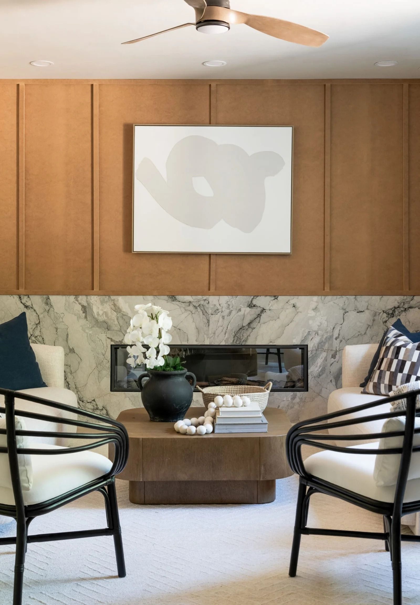 Living room with fireplace, abstract artwork, two black chairs, and beige paneling.