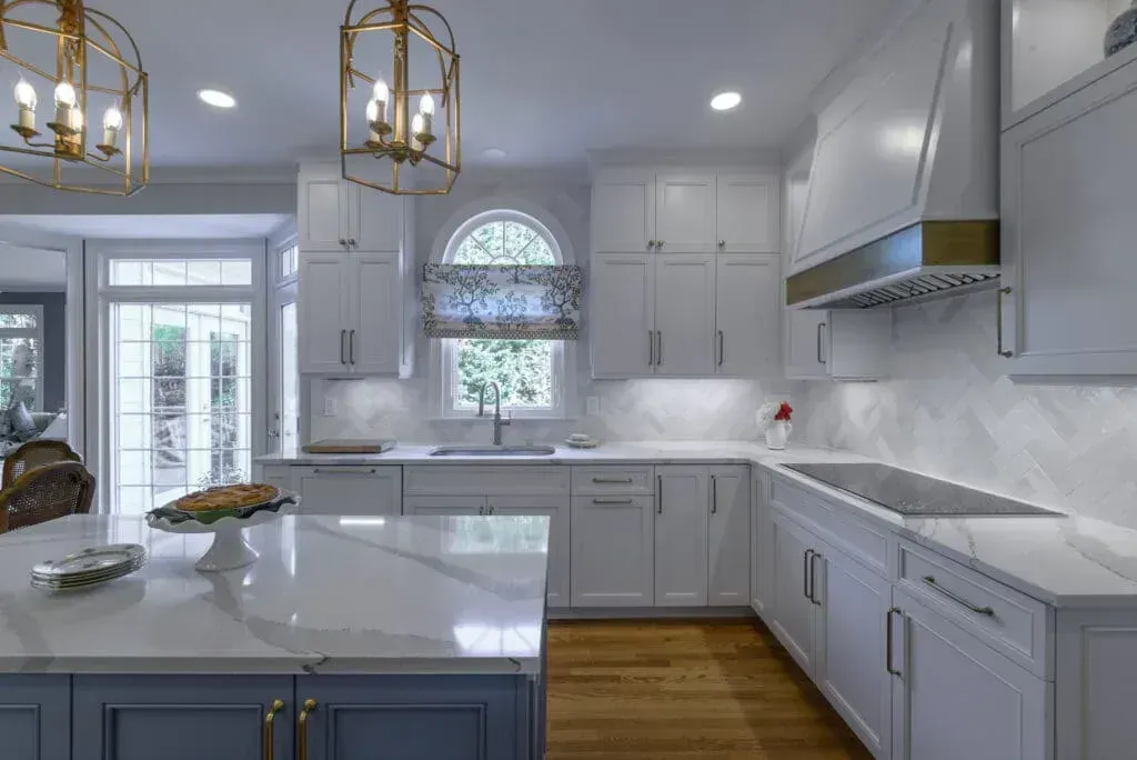 White and blue kitchen with quartz countertops, wood floors, and gold light fixtures.