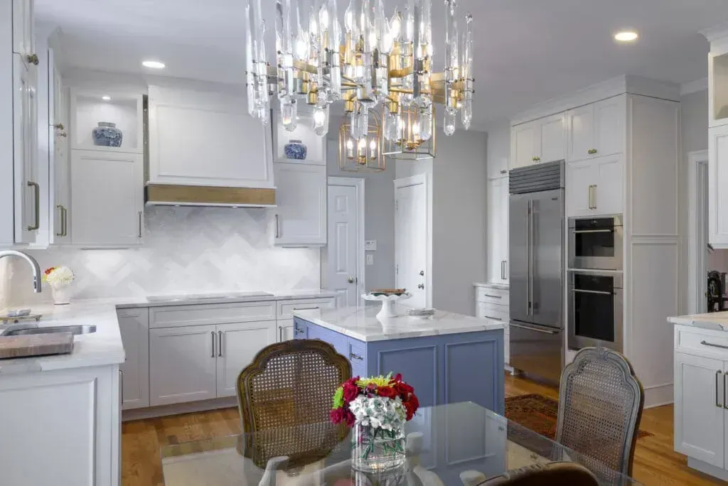 Bright, white kitchen with blue island, chandelier, stainless steel appliances, and dining table.