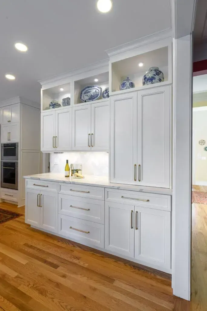 White kitchen cabinets with gold hardware and overhead lighting, displayed on a wooden floor.