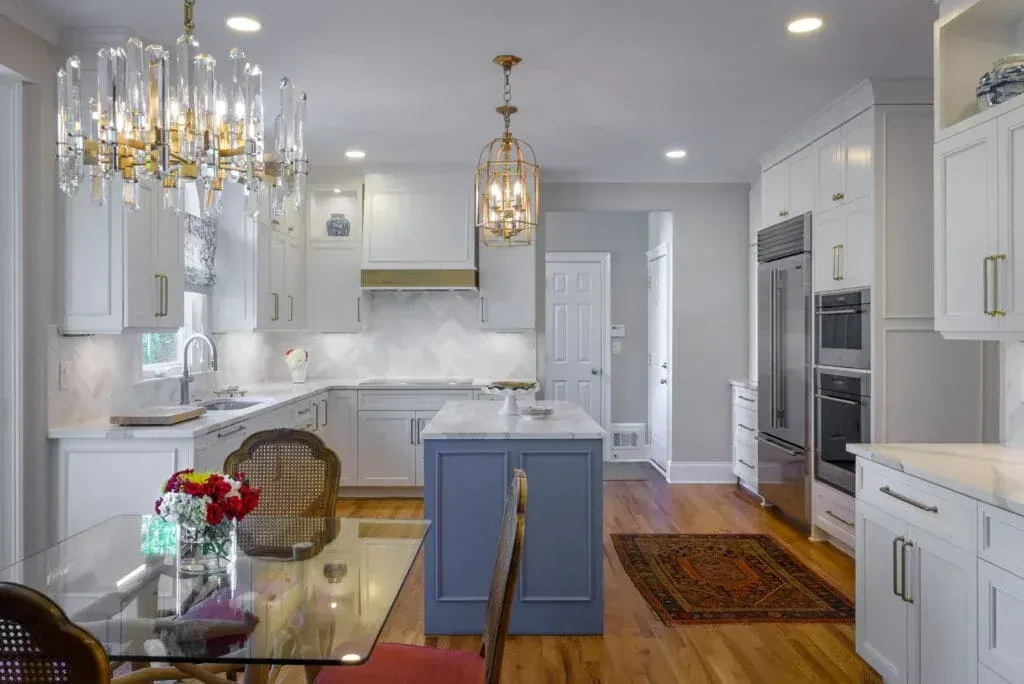 Elegant white kitchen with blue island, gold accents, and a dining table.