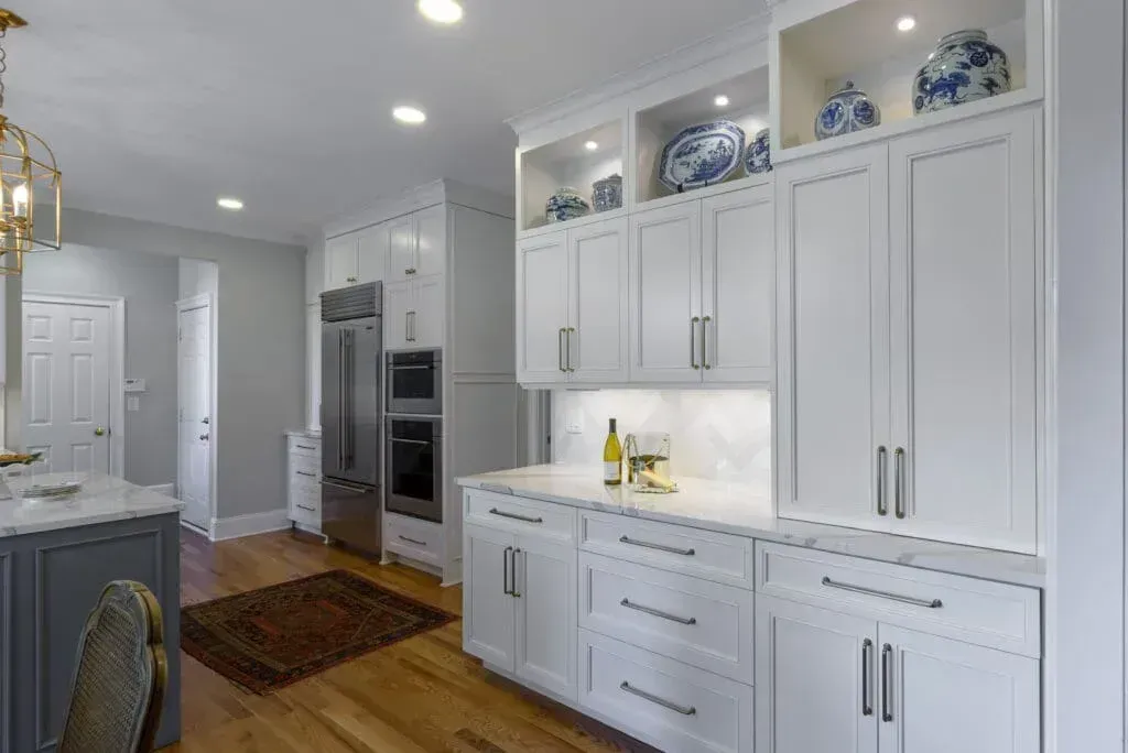 White kitchen cabinets with built-in appliances and lit display shelves.