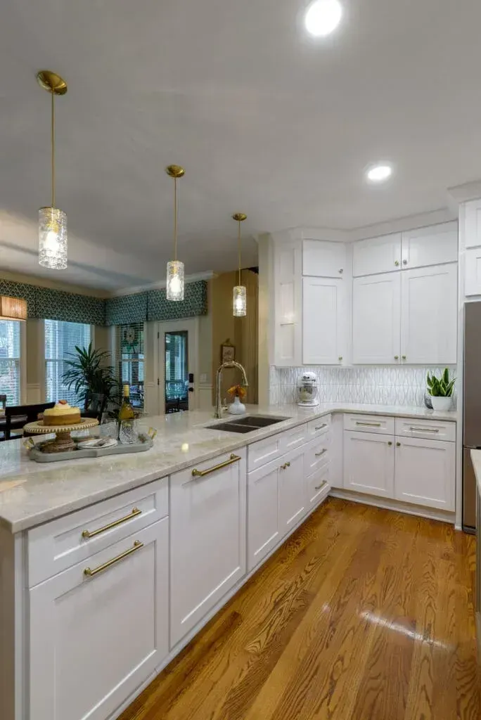 Bright white kitchen with light wood floors, island with sink, and gold pendant lights.
