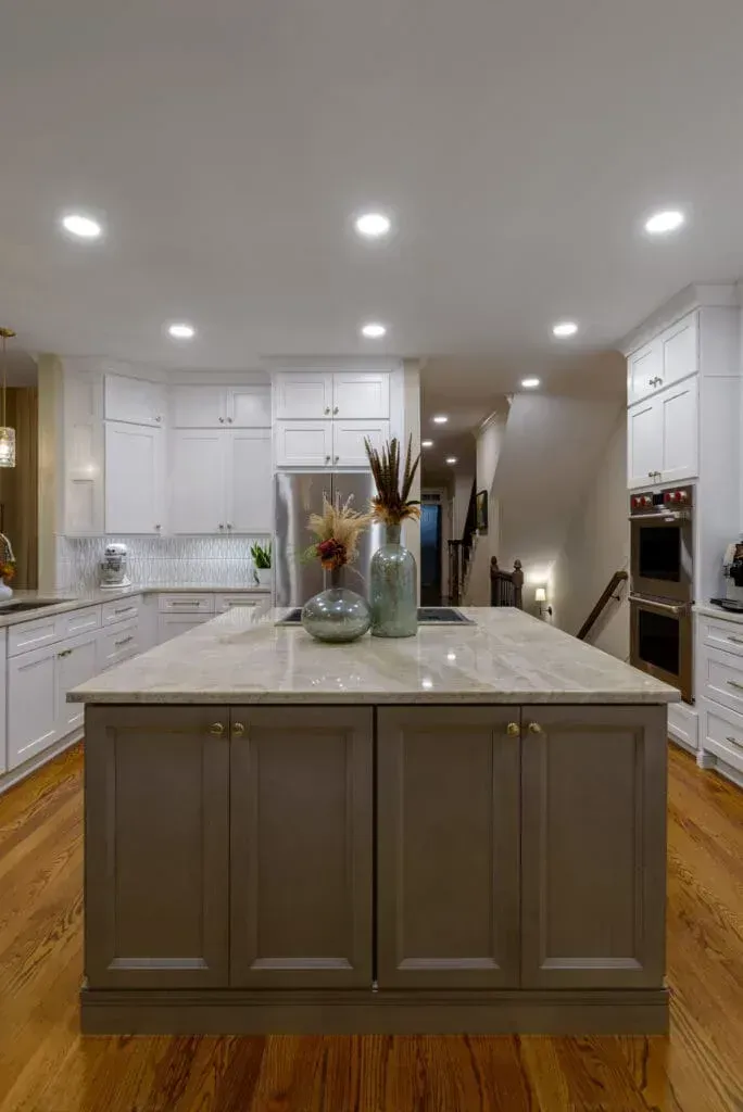 Kitchen with gray island and white cabinets. Wooden floors and recessed lighting.