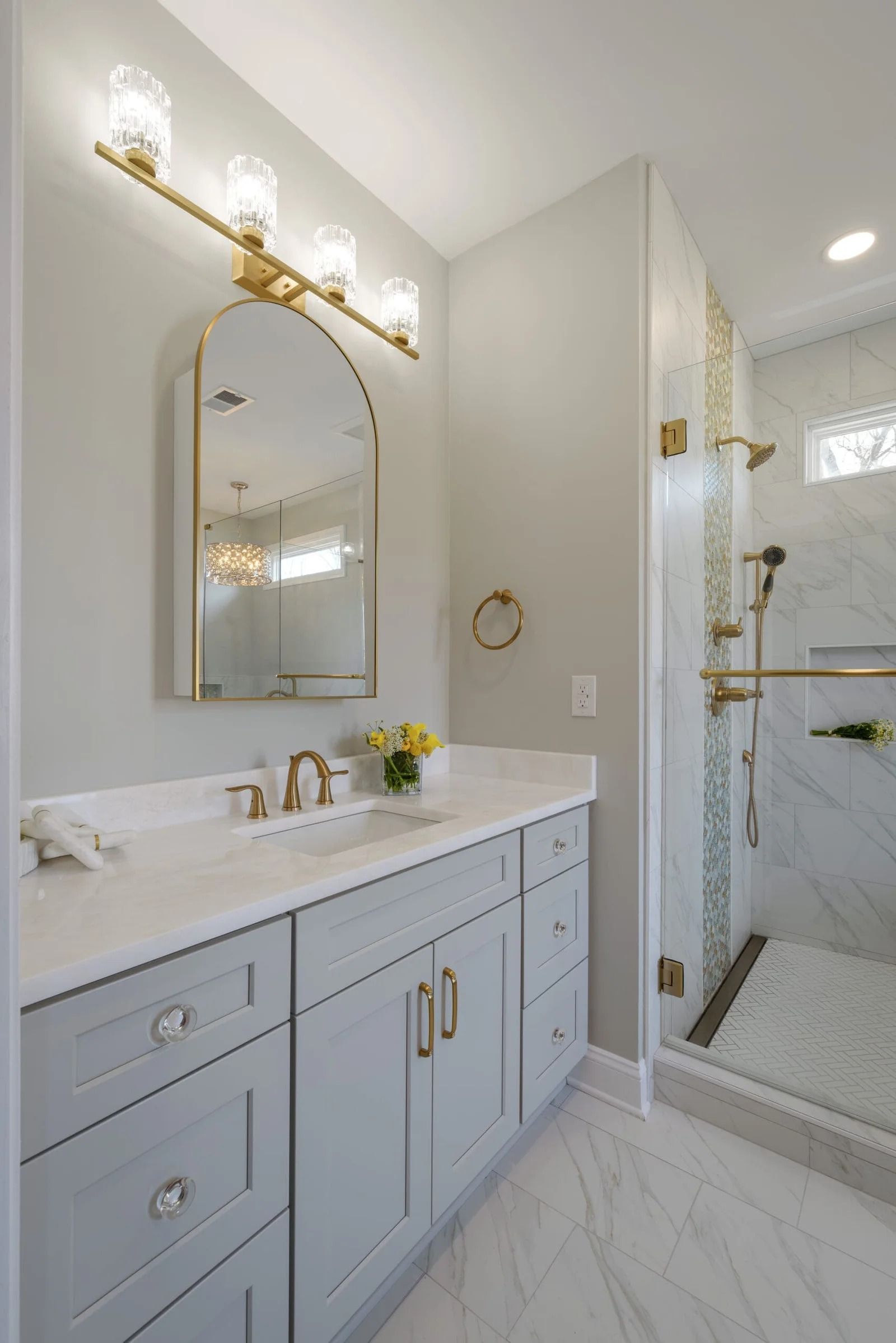 Bathroom with light blue vanity, gold fixtures, arched mirror, and marble shower.