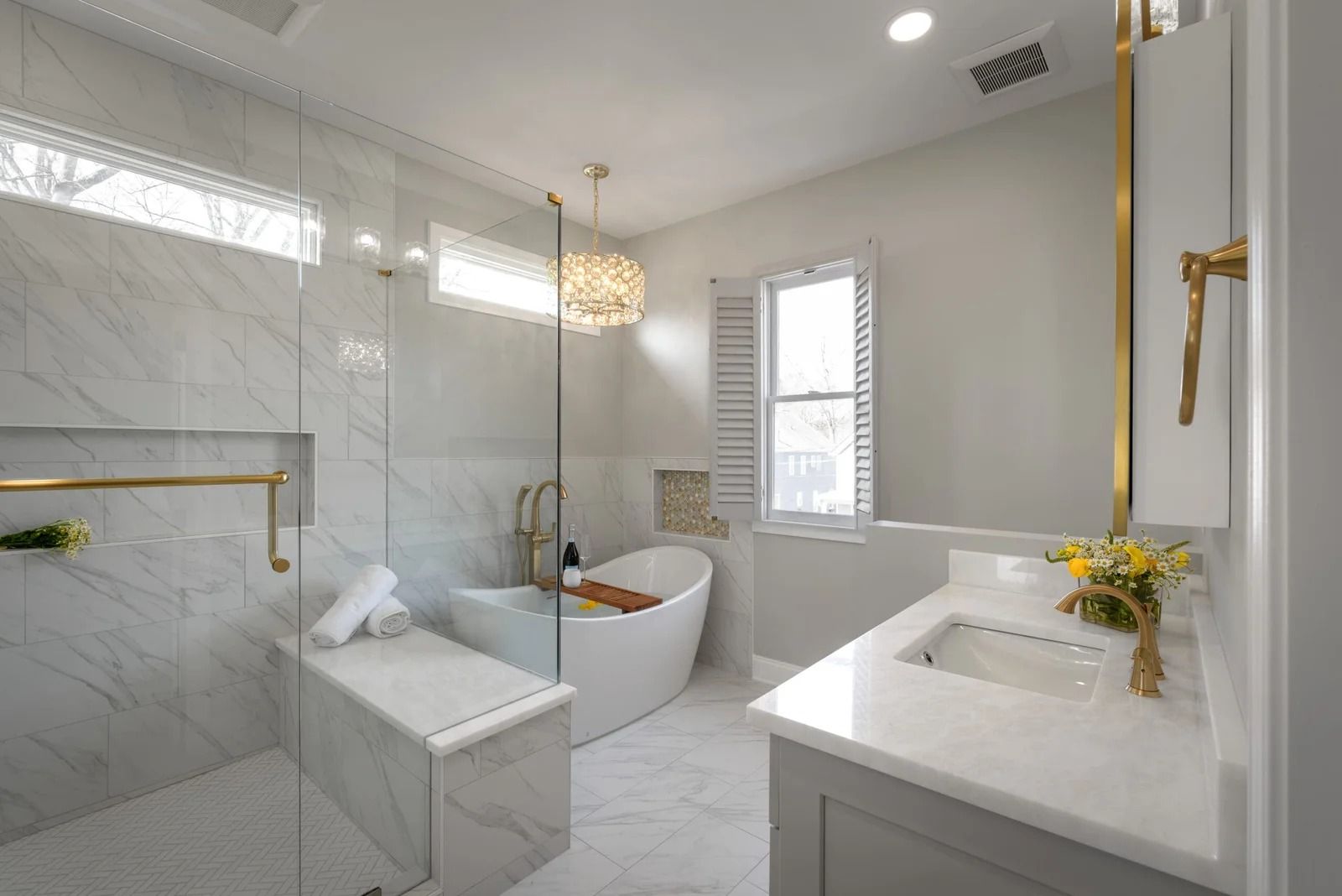 Luxurious white bathroom with marble tile, a freestanding tub, and gold accents.