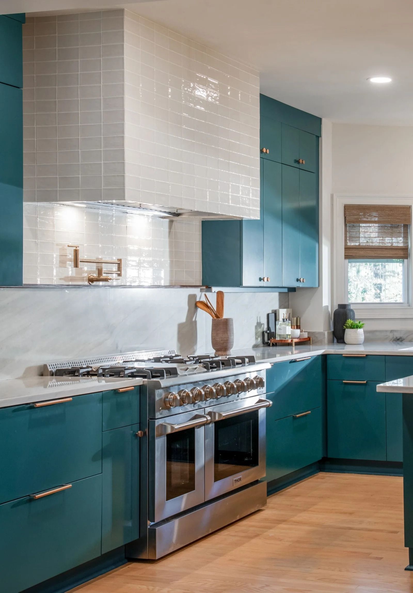 Teal kitchen with stainless steel range, white tile range hood, and light wood flooring.