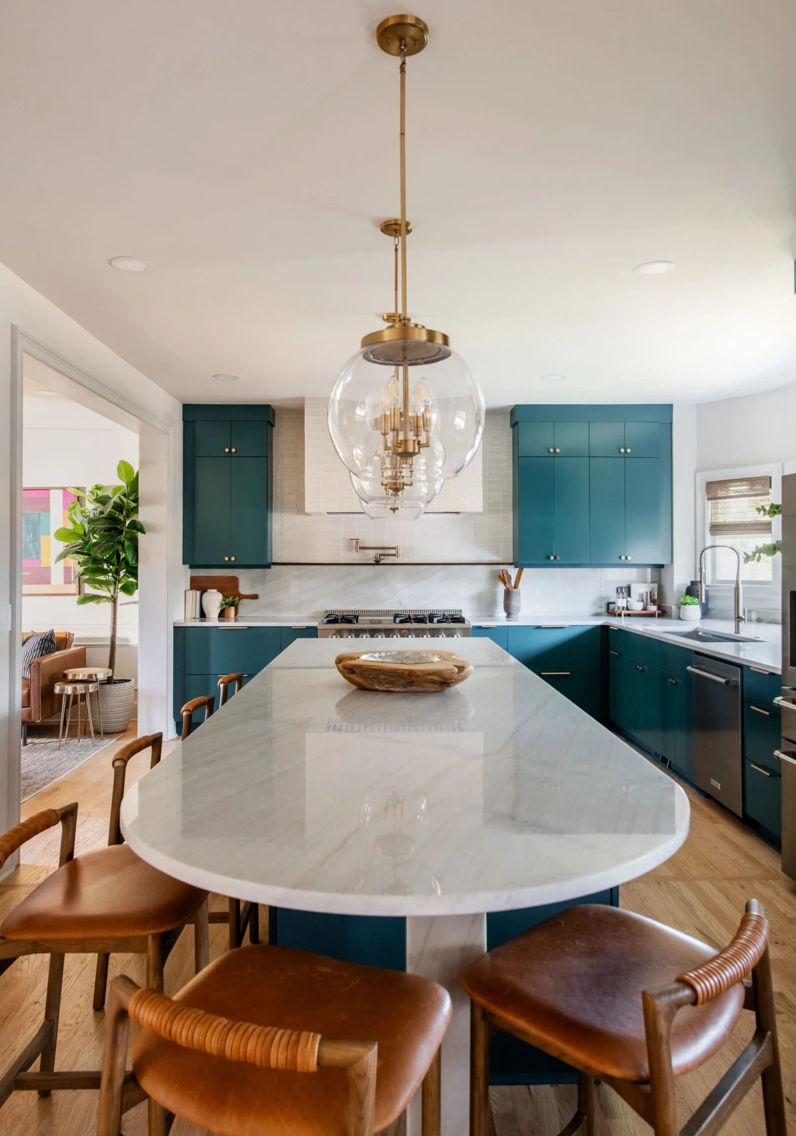 Modern teal kitchen with white marble island, gold pendant light, and leather bar stools.
