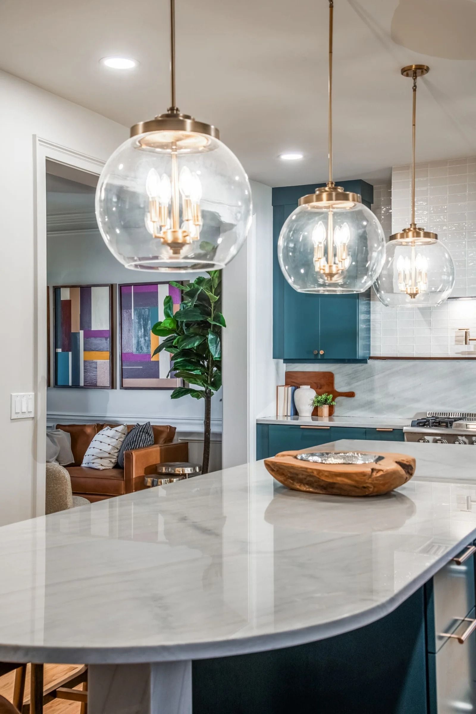 Kitchen island with pendant lights, cabinetry, and a view into a living space with art and a plant.