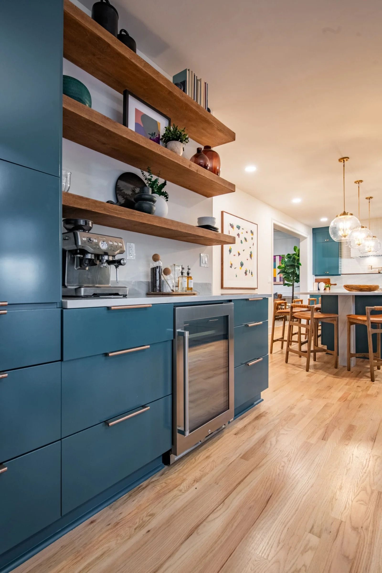 Modern kitchen with teal cabinets, wooden shelves, and a built-in wine fridge.