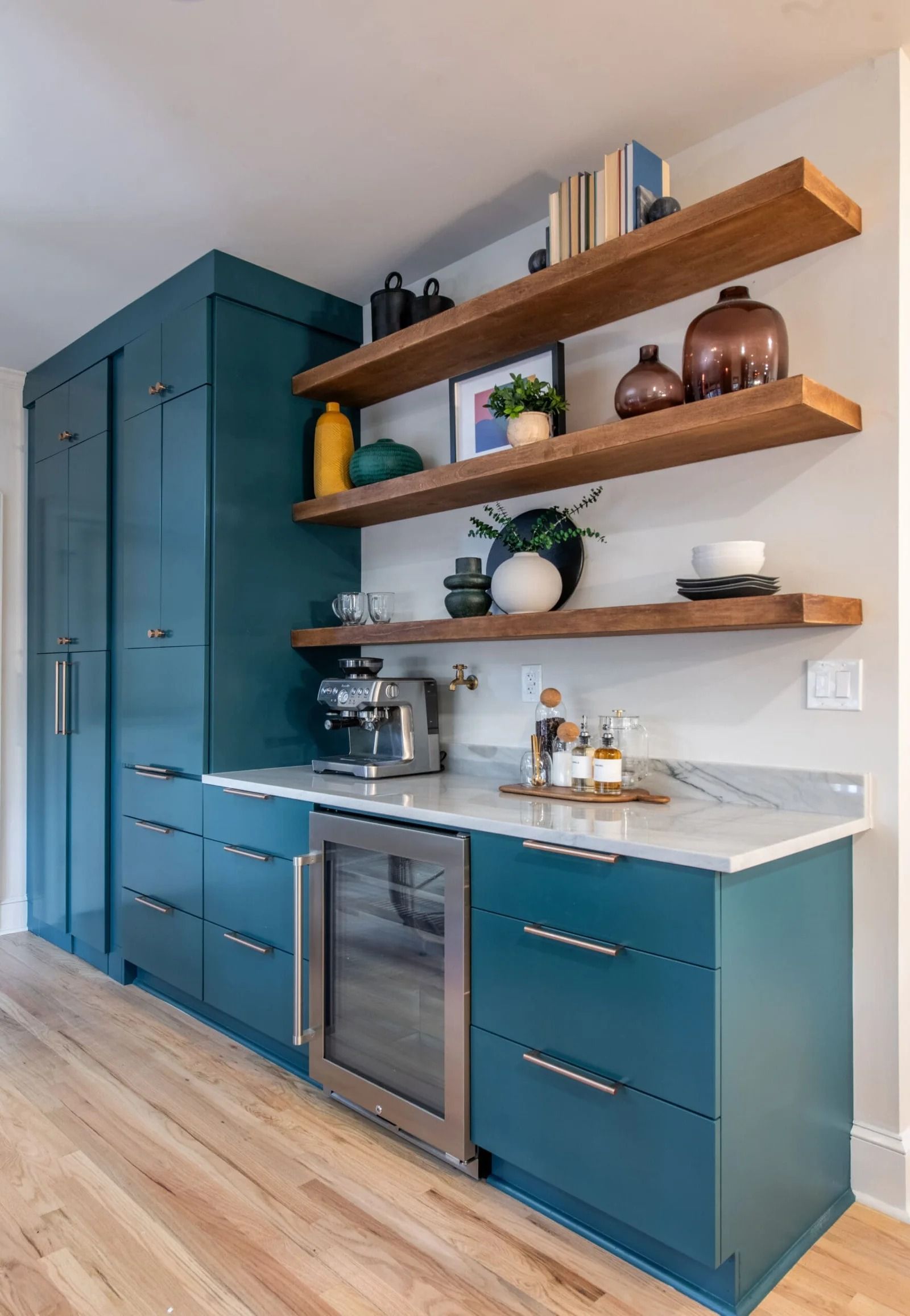Blue built-in bar area with a coffee maker, beverage fridge, open shelving, and decorative items.