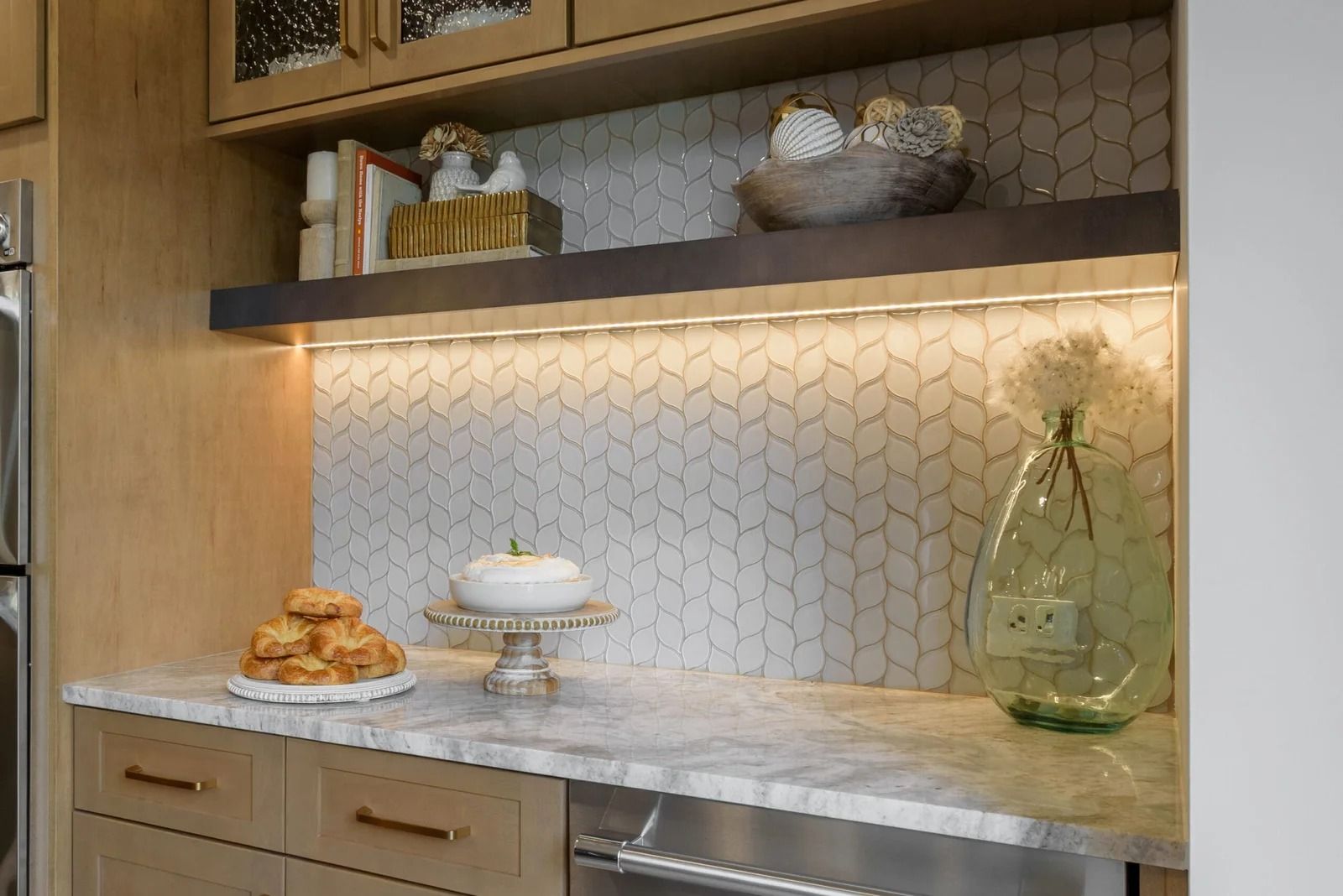 Kitchen with wood cabinets, marble countertop, and backsplash with built-in shelf displaying decor.