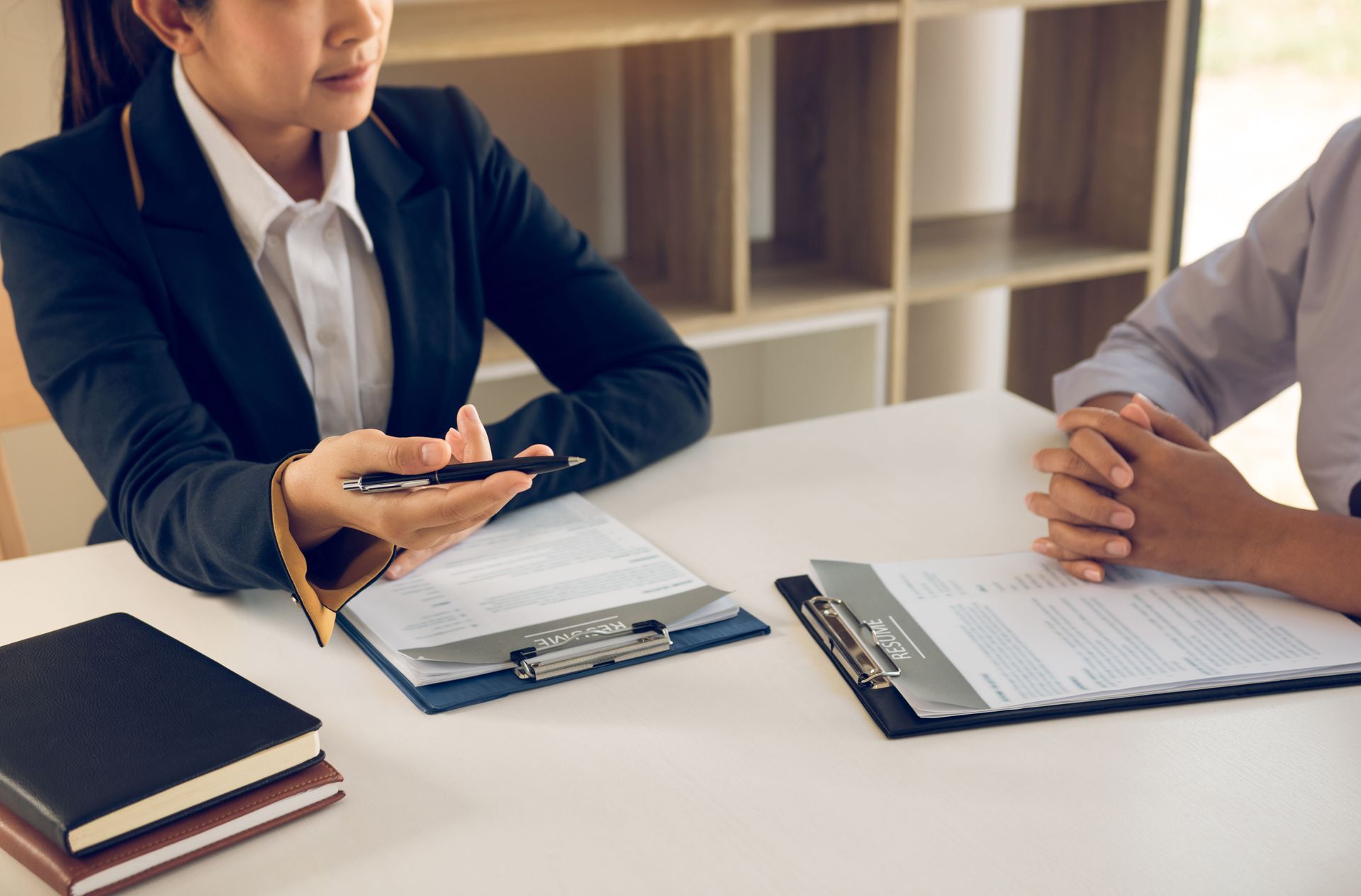 Two people in business attire discussing documents at a conference table with a notebook and clipboard.