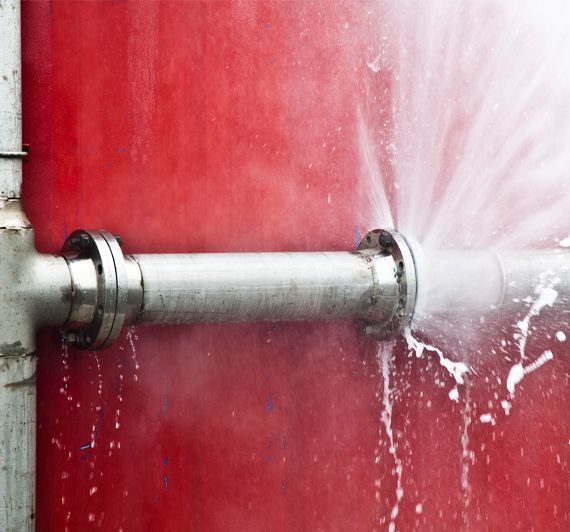 A pipe is leaking water on a red wall.