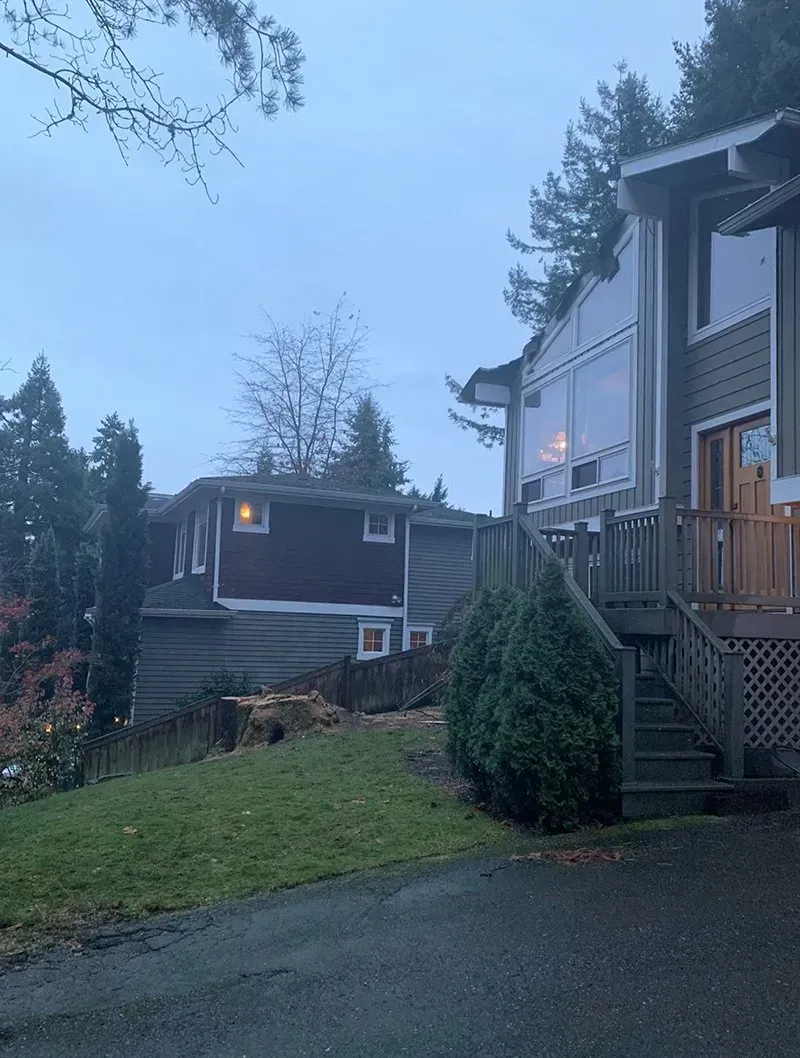 Two houses on a slight hill, one with a deck, overcast sky, grass and trees in the yard.